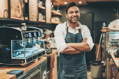 Business Package for Shops Insurance - Smiling barista standing confidently behind a coffee machine inside a modern café.
